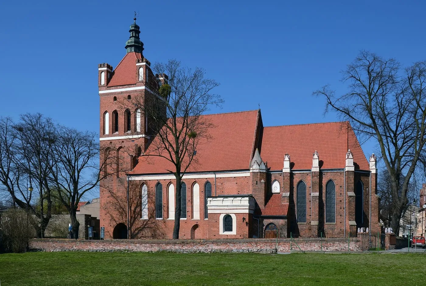 Ceglana, obronna wieża kościoła św. Katarzyny w Golubiu, z czerwonym dachem nawy, wiosną