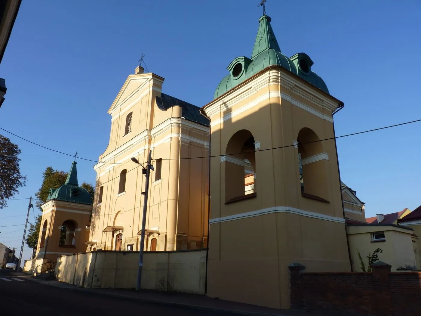 Żółty kościół z dzwonnicą zwieńczoną zielonym, miedzianym hełmem, uchwycony z niskiego kąta w słońcu, na tle intensywnie błękitnego nieba