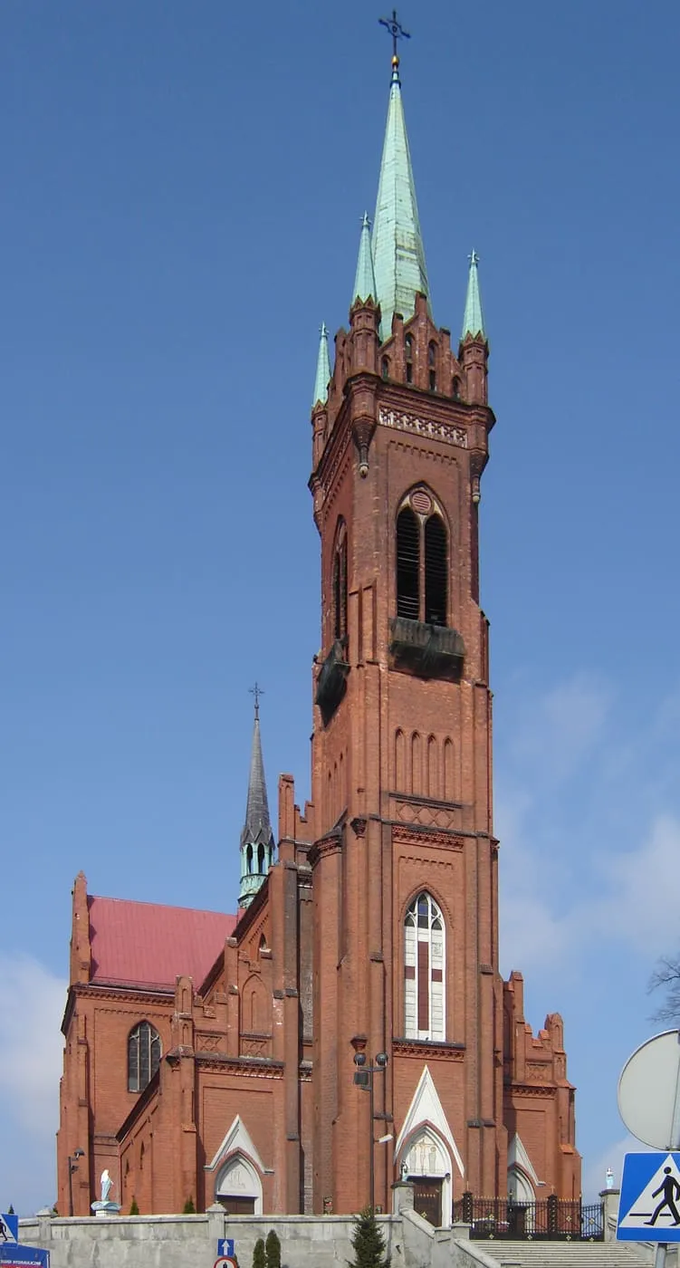 Ceglana, neogotycka wieża kościoła św. Katarzyny w Zgierzu z zieloną iglicą i czterema narożnymi sterczynkami, na tle błękitnego nieba
