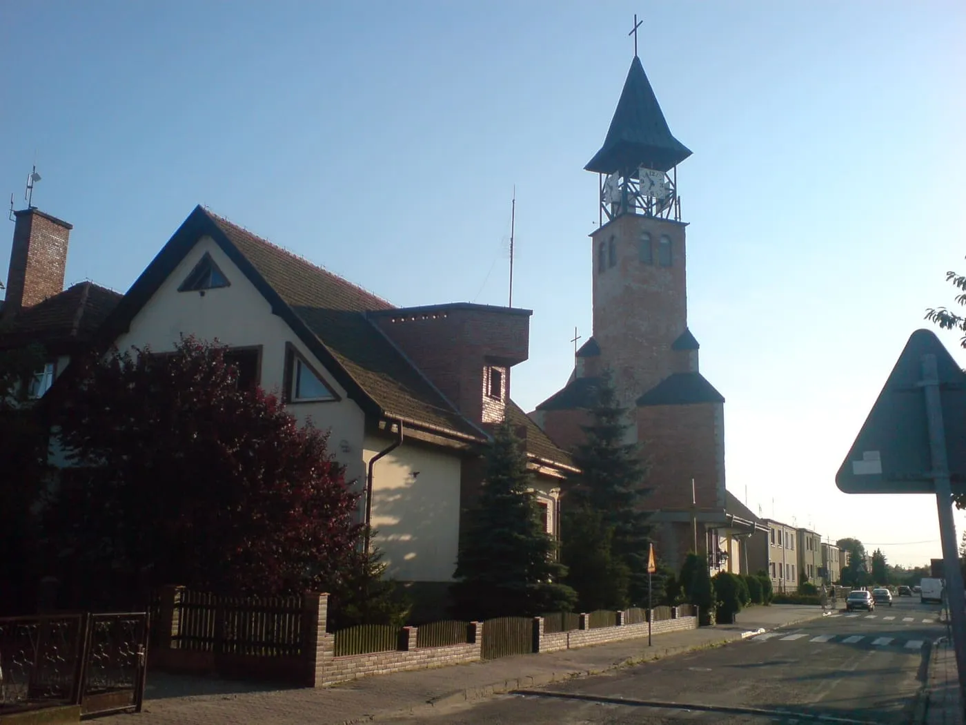 Nowoczesny ceglany kościół z wieżą zegarową, widoczny zza domu o zmierzchu