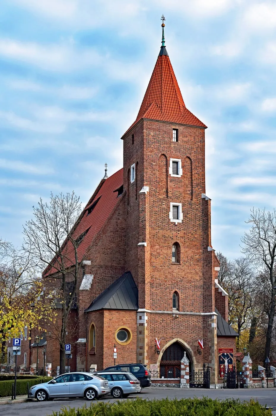 Gotycki kościół Świętego Krzyża w Krakowie z masywną ceglaną wieżą zwieńczoną spiczastym hełmem
