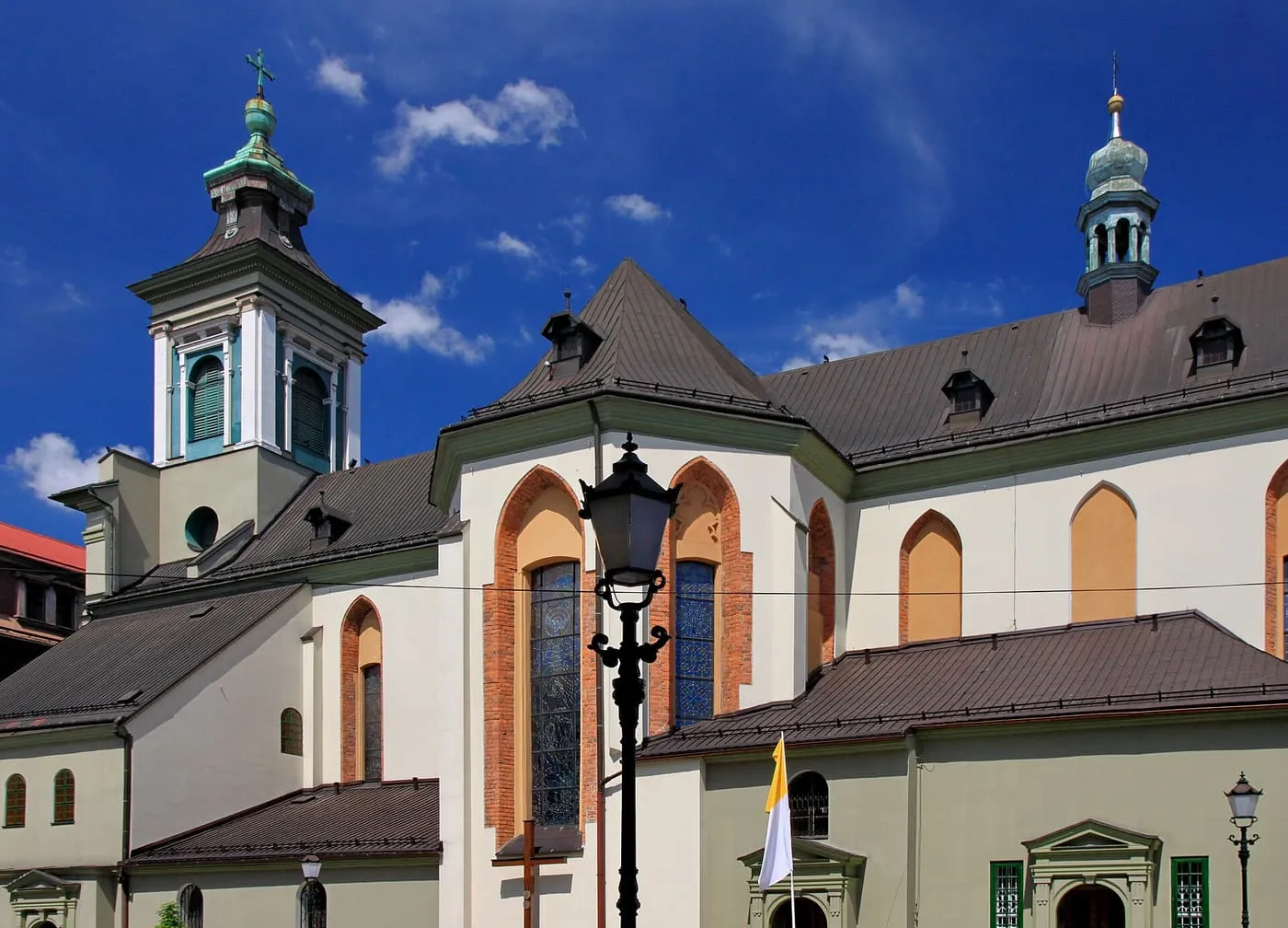 Barokowo-klasycystyczna fasada kościoła św. Marii Magdaleny w Cieszynie z dwiema asymetrycznymi wieżyczkami — zieloną spiczastą i srebrną cebulastą — na tle głębokiego błękitu nieba