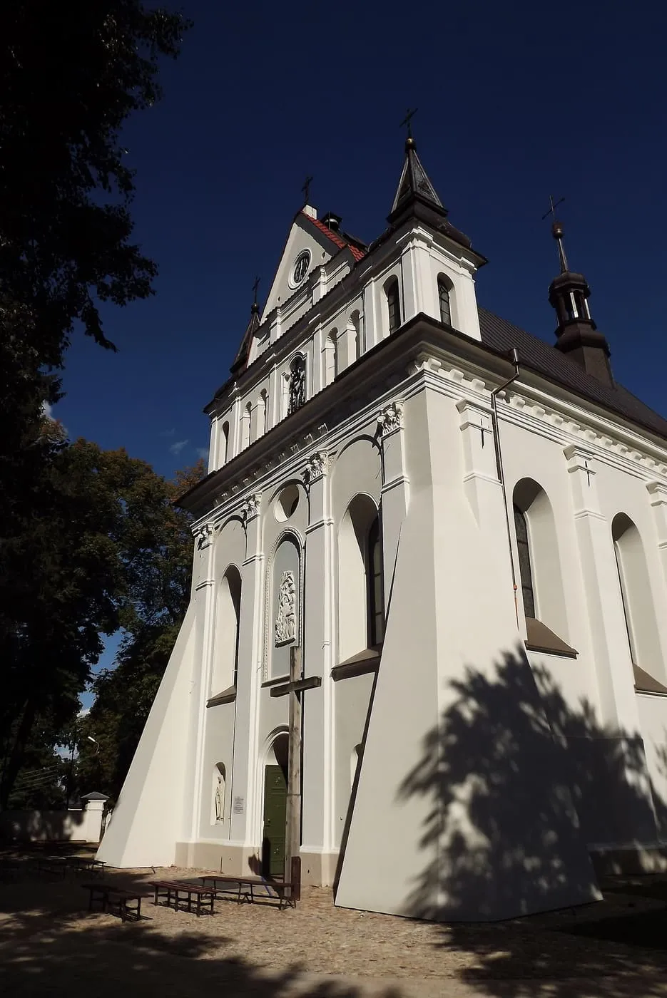 Biała, renesansowa bryła kościoła św. Marii Magdaleny w Łęcznej z trójkątnym szczytem z zegarem i wysoką, ażurową sygnaturką, fotografowana z dołu na tle granatowego nieba
