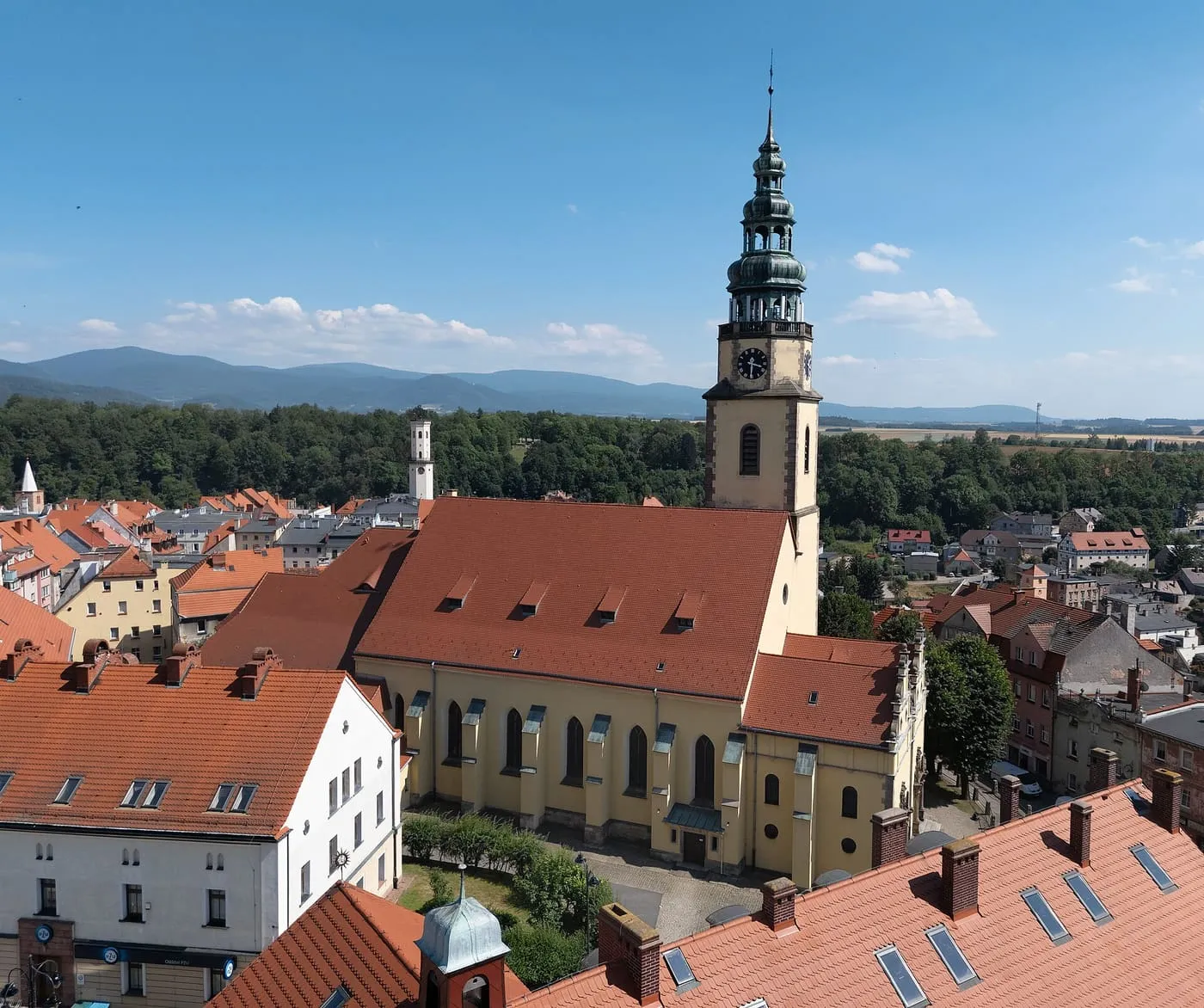 Kościół św. Michała Archanioła w Bystrzycy Kłodzkiej widziany z lotu ptaka, z kremową wieżą zwieńczoną zieloną, wielopiętrową barokową kopułą, nad czerwonymi dachami starówki