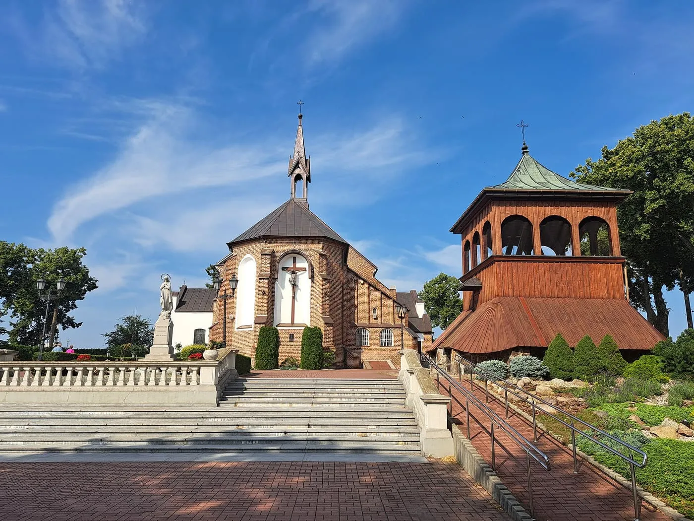 Ceglany kościół św. Mikołaja w Grójcu z krucyfiksem na fasadzie, obok drewnianej dzwonnicy