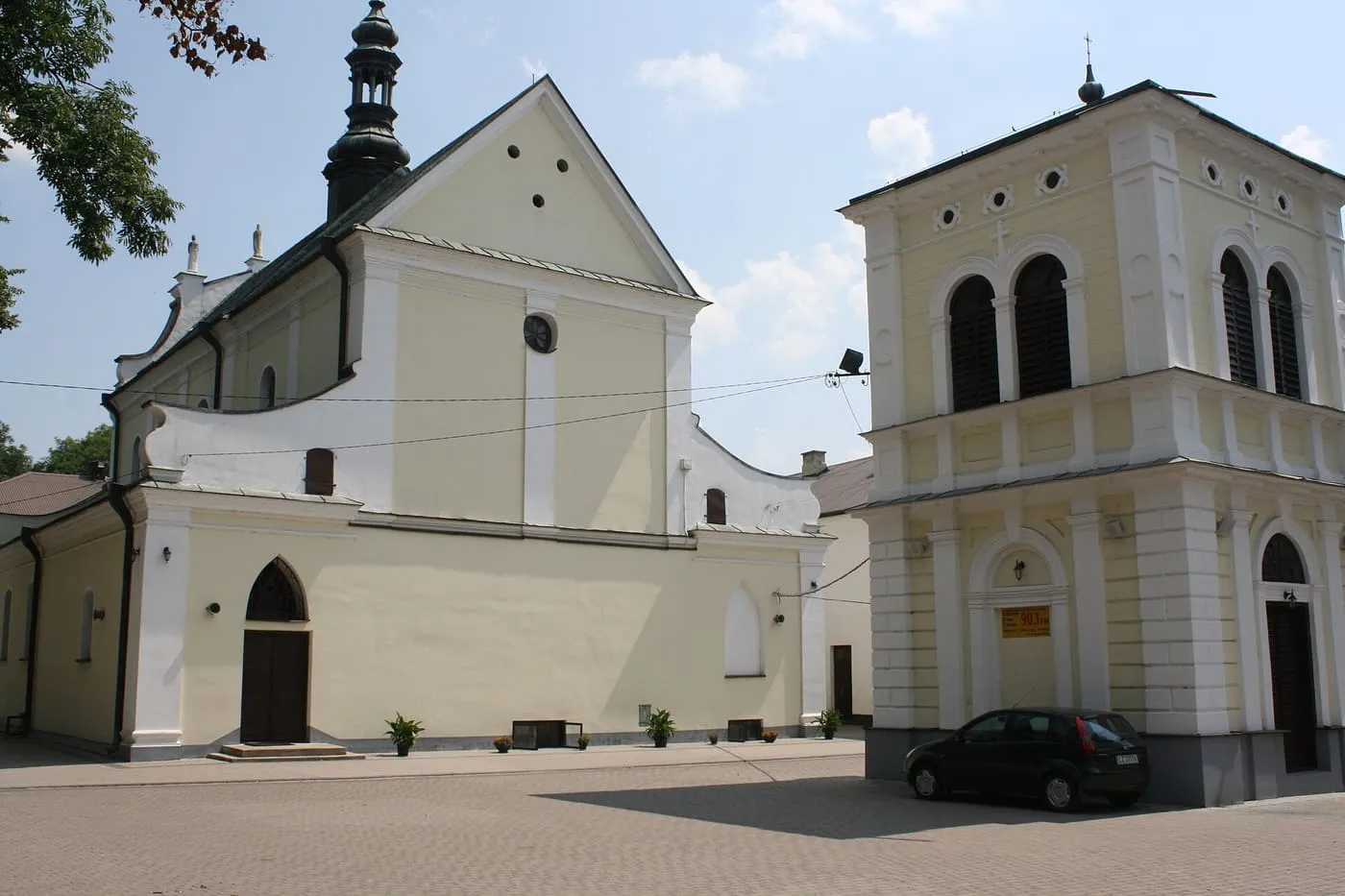 Kremowa, barokowa fasada kościoła św. Mikołaja w Hrubieszowie z ciemną, cebulastą kopułą wieży, obok osobno stojącej dzwonnicy