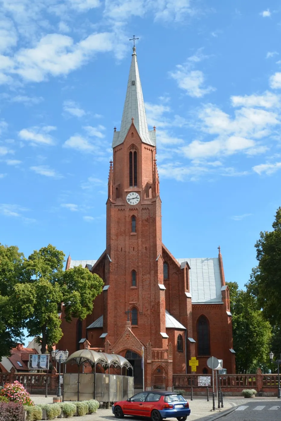 Wysoka, ceglana wieża neogotyckiego kościoła św. Mikołaja w Wałczu, zwieńczona spiczastym hełmem, na tle błękitnego nieba