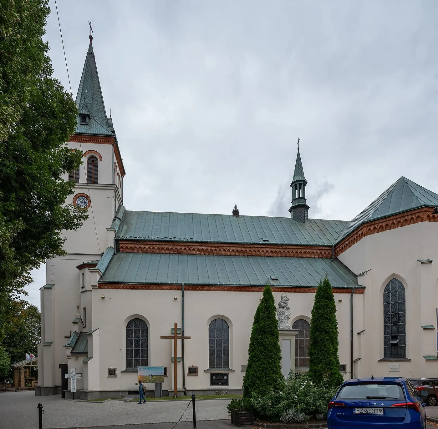 Biała wieża łańcuckiej fary z balkonem i zegarem, obok czerwonego dachu kaplicy z obrazem Matki Bożej Szkaplerznej
