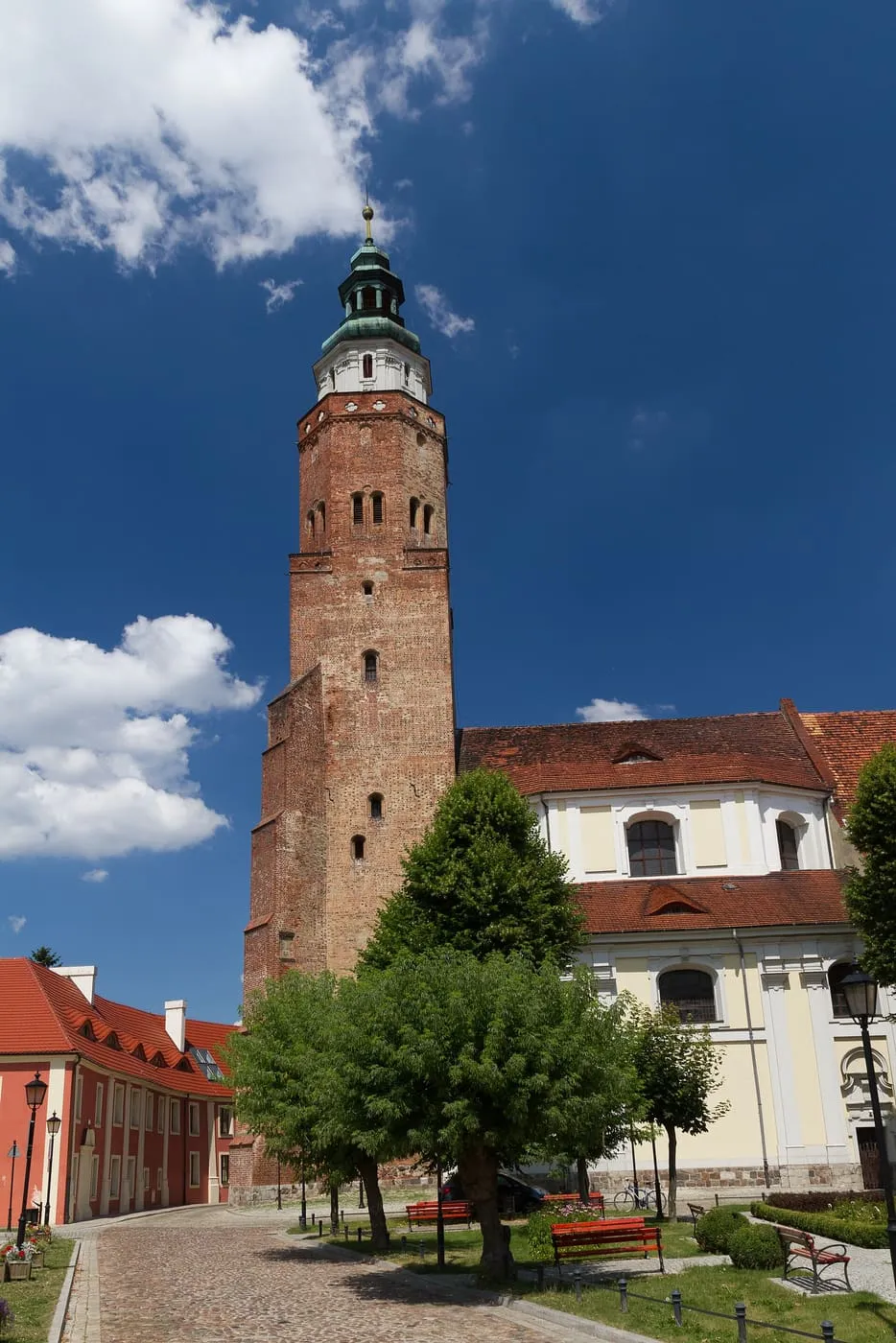 Ceglana wieża fary wschowskiej zwieńczona barokowym hełmem, obok białe zabudowania kościoła