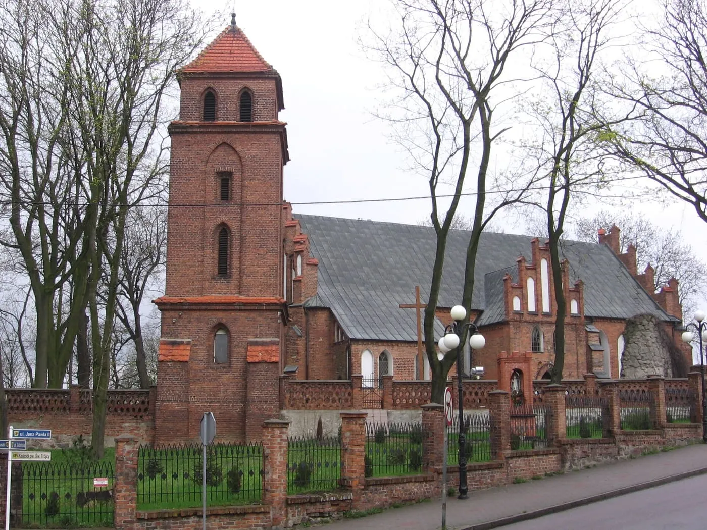 Ceglana, gotycka wieża kościoła Świętej Trójcy w Rypinie z piramidalnym dachem i bliźniaczymi oknami dzwonnymi, połączona ze schodkowym szczytem nawy i murowanym ogrodzeniem cmentarza
