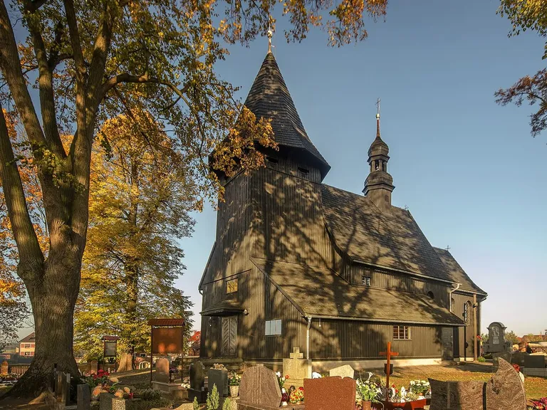Drewniany kościół św. Wawrzyńca w Laskowicach w złotym świetle zachodzącego słońca, otoczony cmentarzem