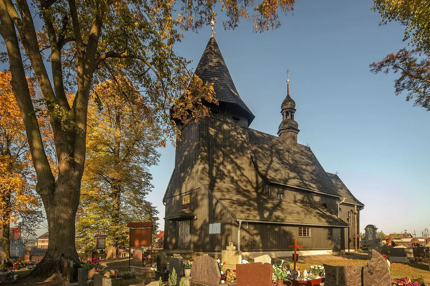 Drewniany kościół św. Wawrzyńca w Laskowicach w złotym świetle zachodzącego słońca, otoczony cmentarzem