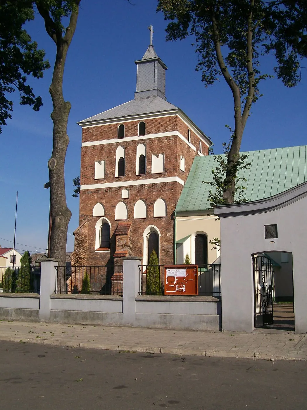 Ceglana wieża fary w Sierpcu zwieńczona spiczastym dachem, na tle głębokiego błękitu nieba