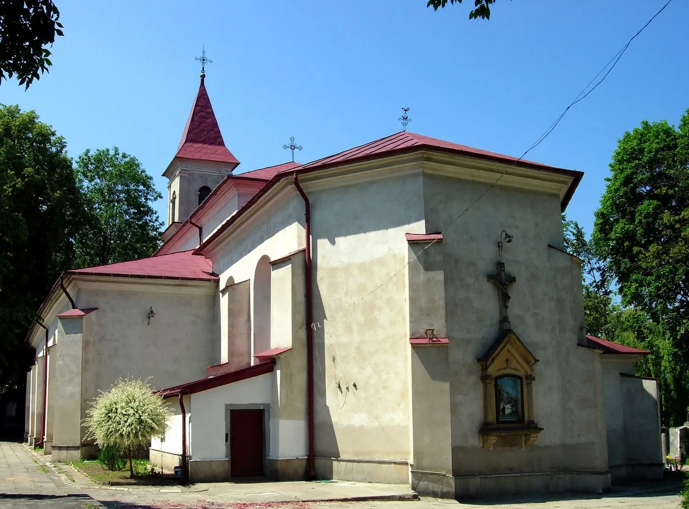Beżowa, barokowa bryła kościoła św. Władysława w Kunowie z niewielką wieżą zwieńczoną bordową iglicą i kapliczką z krucyfiksem wmurowaną w ścianę prezbiterium