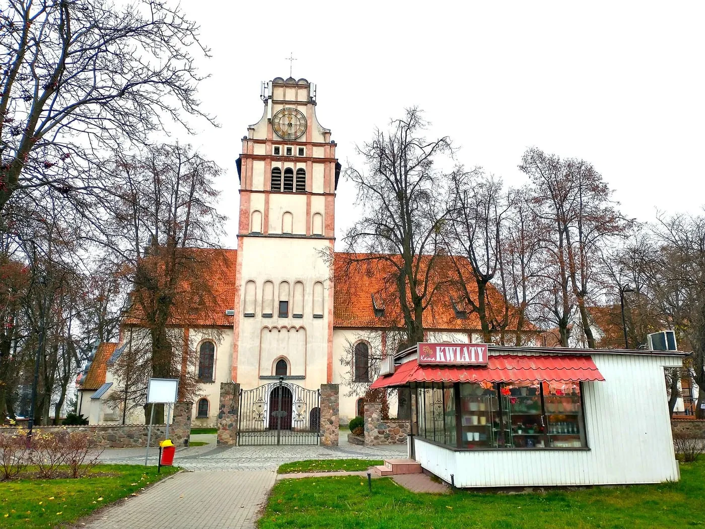 Kościół św. Wojciecha w Nidzicy ze stopniowaną wieżą w kolorze kremowym z różowymi akcentami, wśród bezlistnych drzew