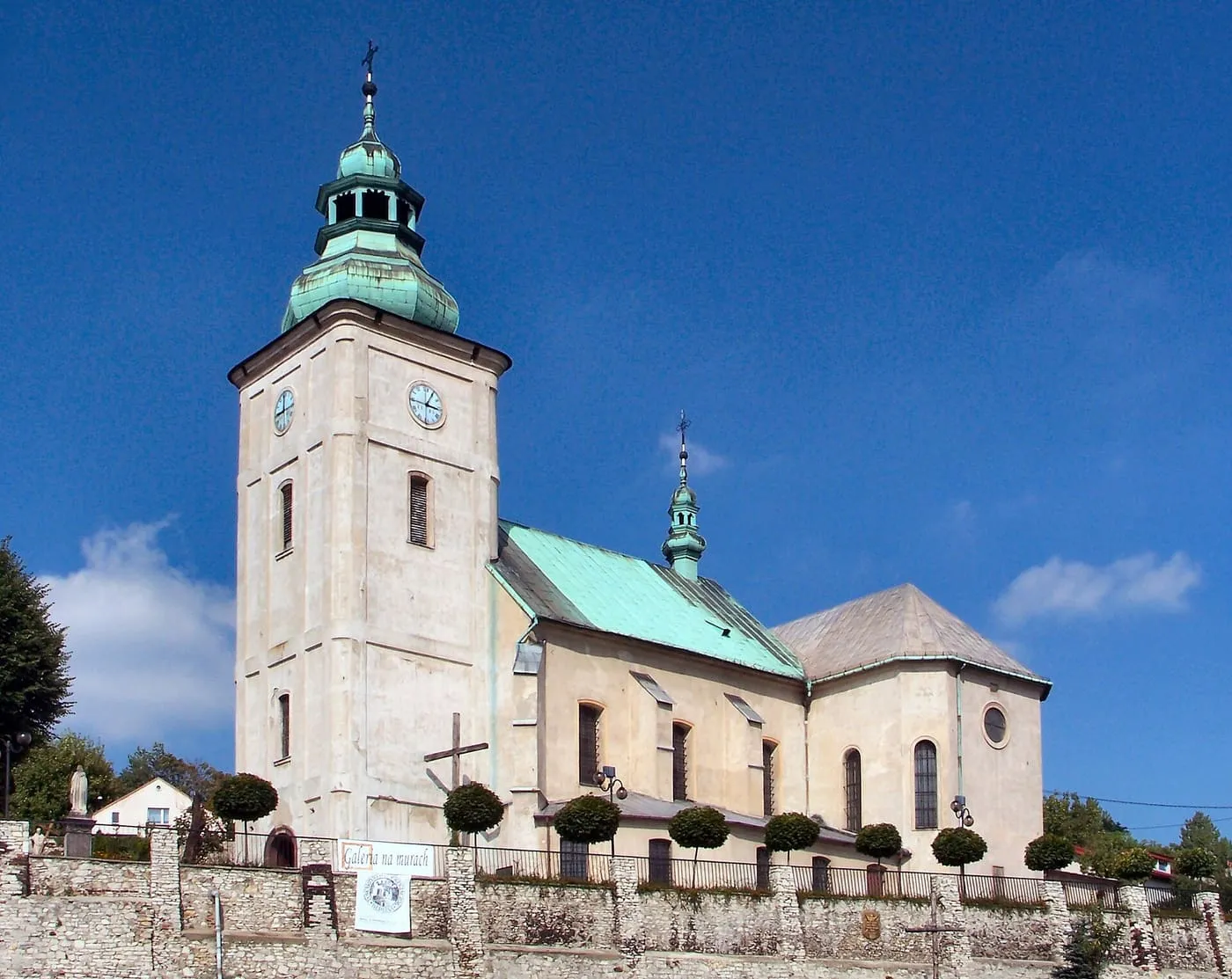 Kamienny kościół Trójcy Przenajświętszej w Będzinie na wzgórzu zamkowym, z wieżą zwieńczoną zieloną, miedzianą kopułą i zegarem, za murem obronnym