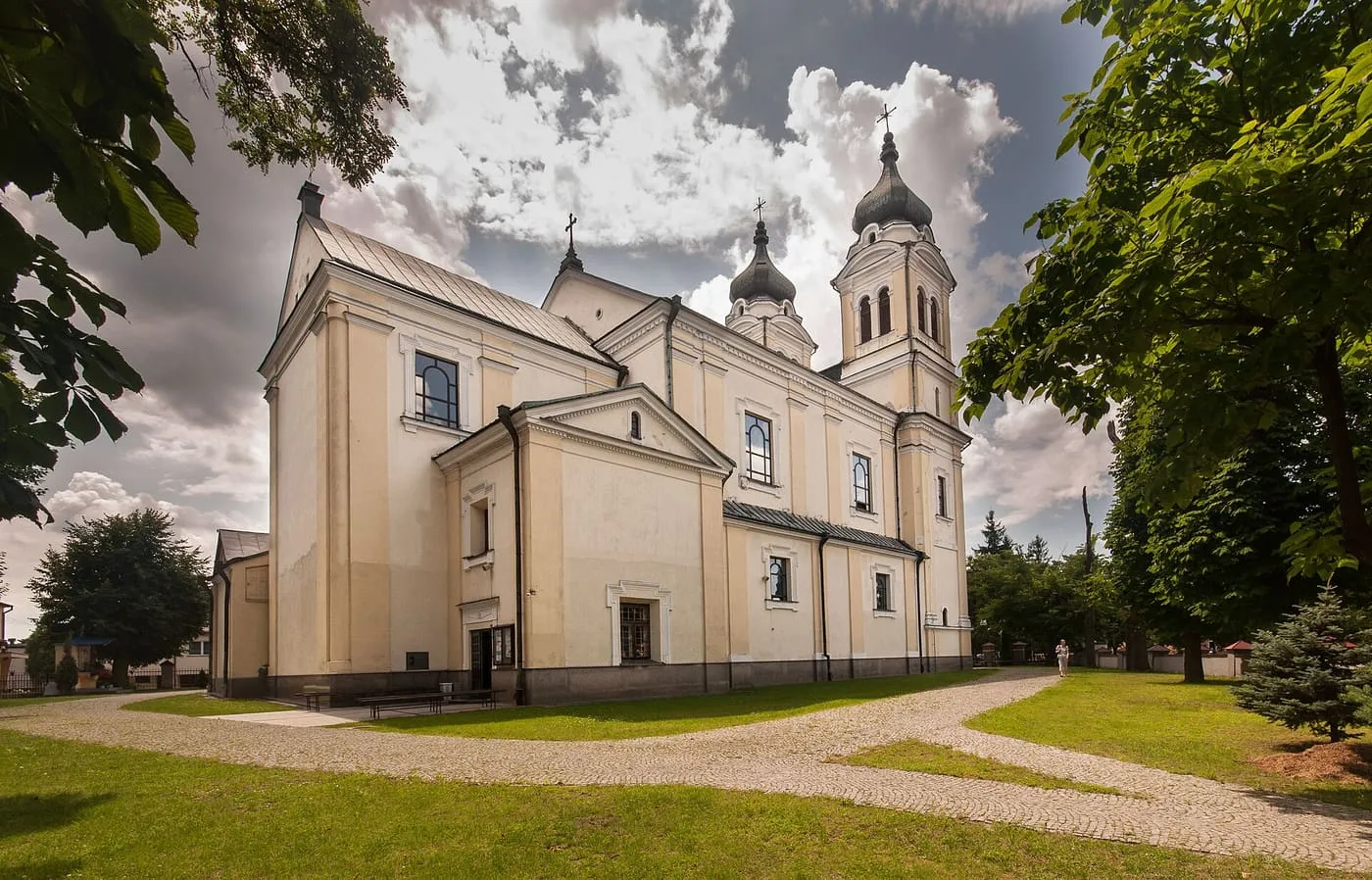 Kremowa, barokowa fasada kościoła Trójcy Świętej i Wniebowzięcia NMP w Biłgoraju z dwiema wieżami zwieńczonymi ciemnymi hełmami