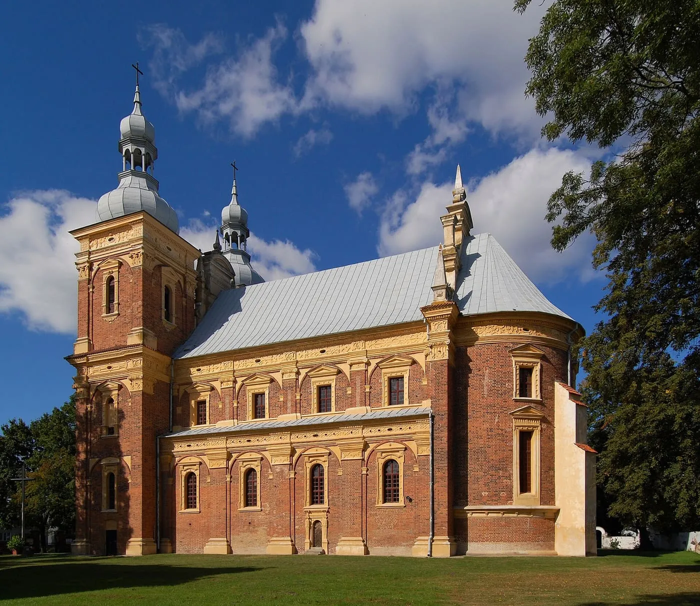 Manierystyczny kościół w Gołębiu z ceglanymi ścianami i bogatą, jasną dekoracją architektoniczną, z wieżami nakrytymi srebrzystymi, cebulastymi hełmami z latarniami