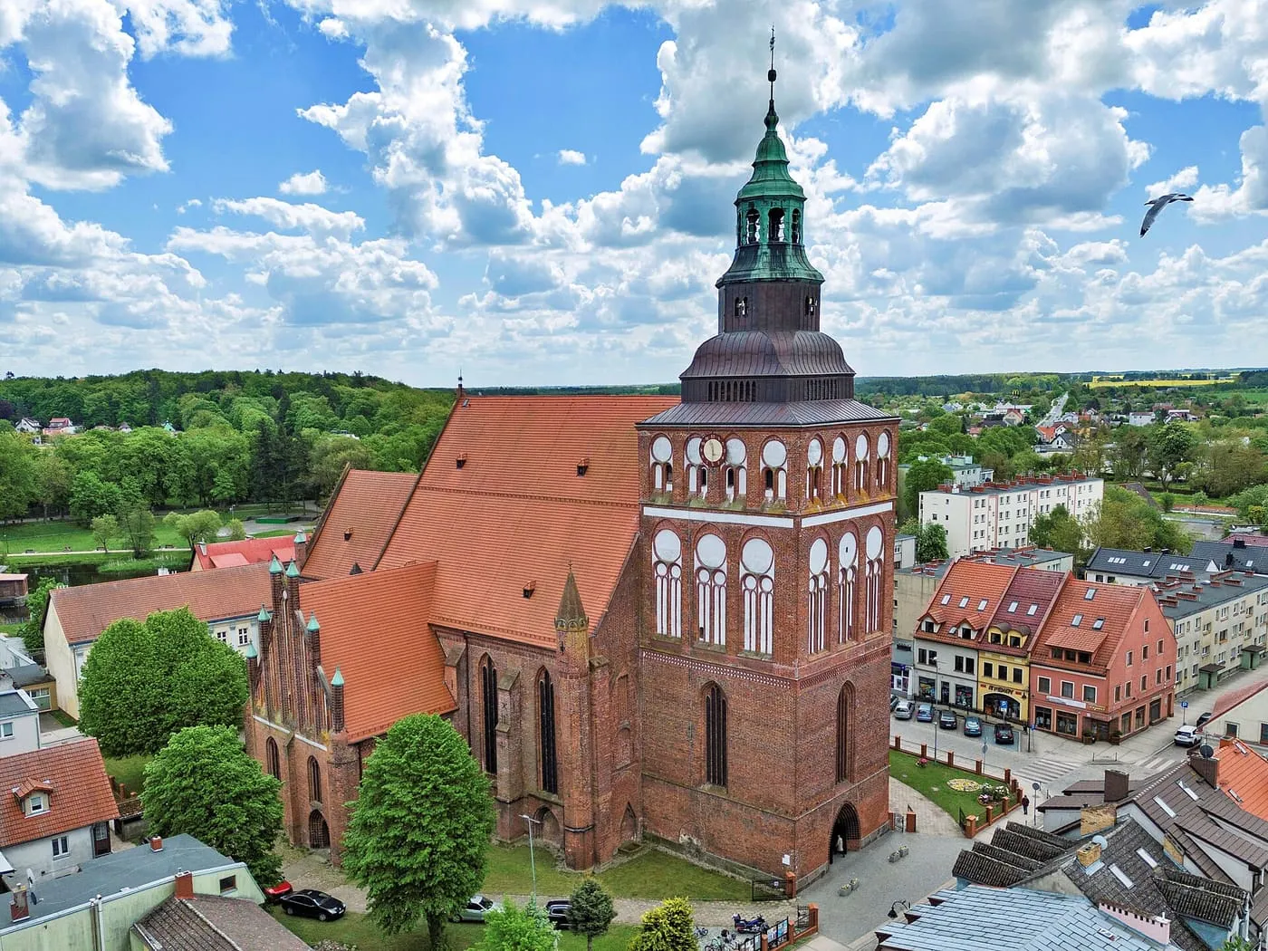 Gotycka, ceglana fara w Gryficach z lotu ptaka, z masywną wieżą ozdobioną białymi blendami i zwieńczoną zielonym, ażurowym hełmem, obok szczyt kaplicy z pinaklami
