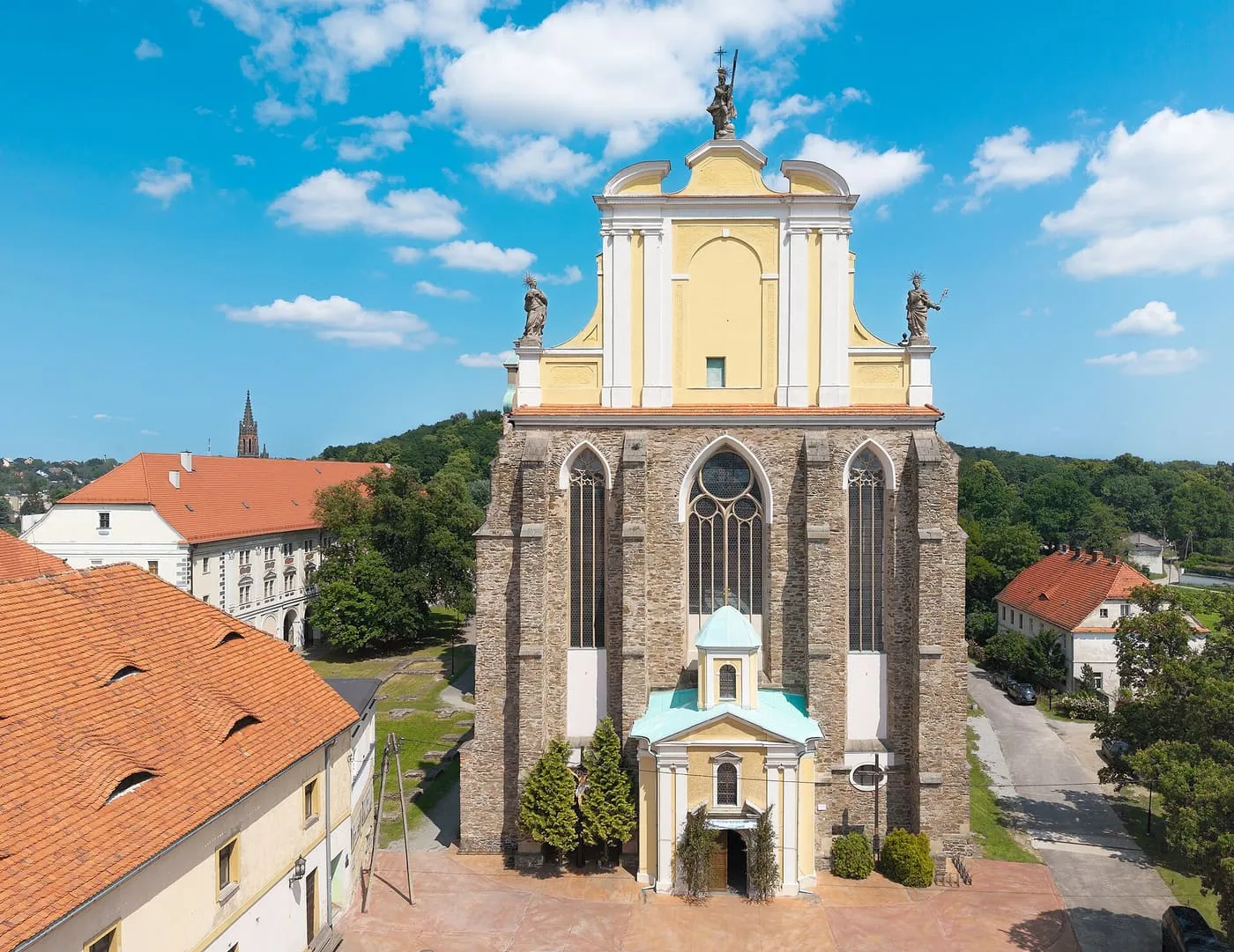 Widok z lotu ptaka na gotycką wieżę kościoła w Kamieńcu Ząbkowickim z barokowym, żółto-białym szczytem zwieńczonym figurami świętych, wśród czerwonych dachów zabudowań klasztornych