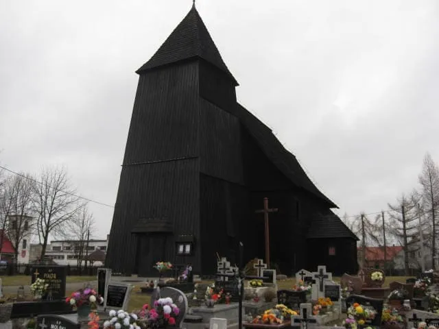 Niewielki, czarny kościół drewniany w Lasowicach Małych, otoczony grobami cmentarnymi