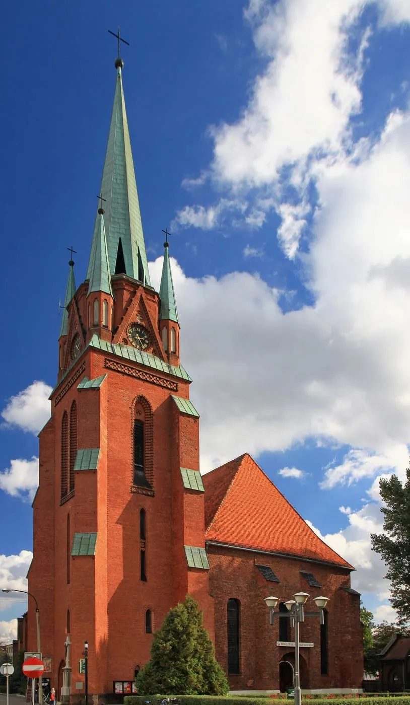 Wysoka, ceglana wieża kościoła Wniebowzięcia NMP w Raciborzu ze smukłą, zieloną iglicą i czterema narożnymi sterczynkami