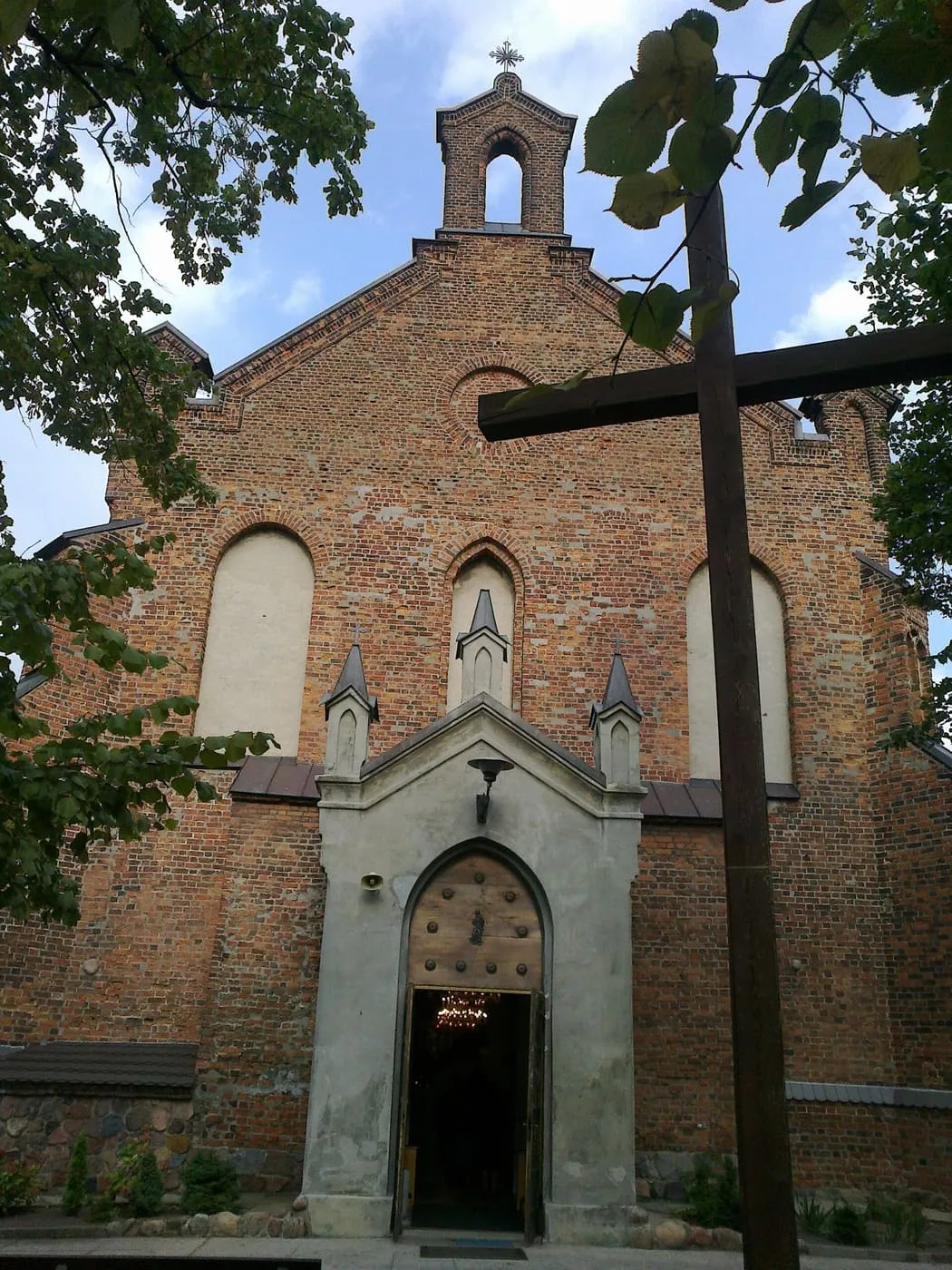 Ceglany, gotycki kościół w Radziejowie z kwadratową wieżą zwieńczoną spiczastym dachem, pod pochmurnym niebem