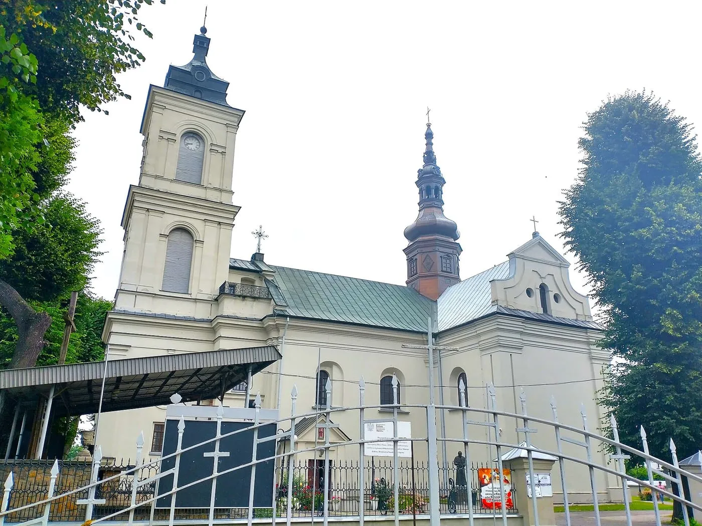 Jasnożółty kościół Wniebowzięcia NMP we Włoszczowie z kwadratową wieżą zegarową i ośmioboczną, ceglaną dzwonnicą zwieńczoną smukłą iglicą