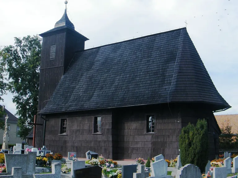 Drewniany kościół Wszystkich Świętych w Lasowicach Wielkich ze stromą wieżą, wśród cmentarnych krzyży