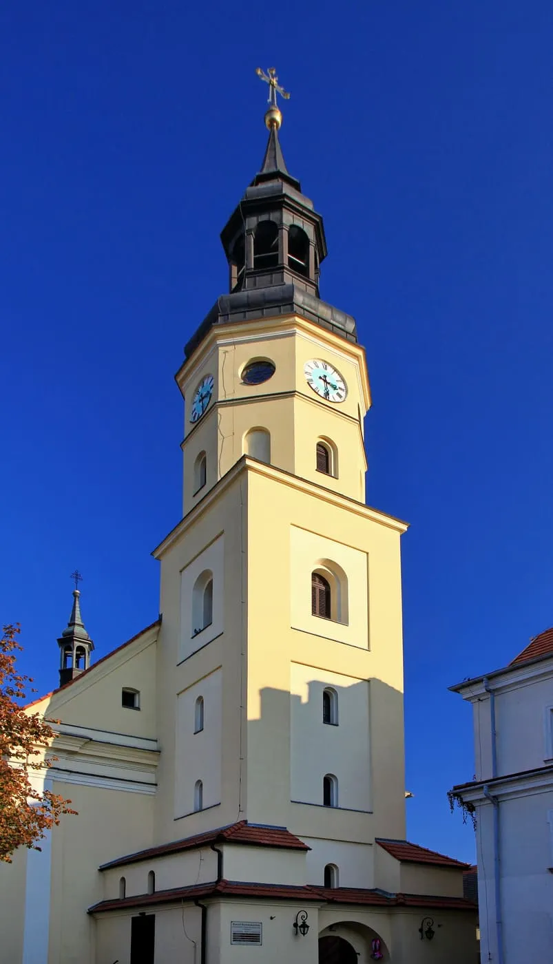 Kremowa wieża kościoła Wszystkich Świętych w Pszczynie z ciemną, ośmioboczną latarnią i zegarem, na tle głębokiego błękitu nieba