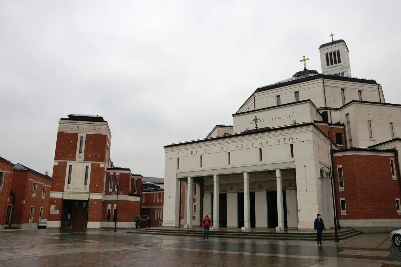 Fasada Sanktuarium św. Jana Pawła II w Krakowie z napisem „Aperite portas Christo” nad kolumnowym wejściem, po lewej ceglany budynek Veritas z Muzeum św. Jana Pawła II, w tle wieża z krzyżem