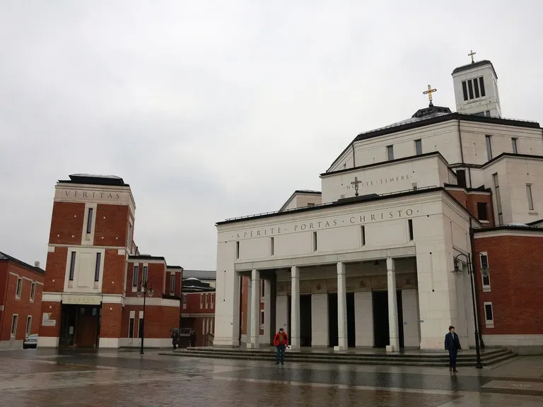 Fasada Sanktuarium św. Jana Pawła II w Krakowie z napisem „Aperite portas Christo” nad kolumnowym wejściem, po lewej ceglany budynek Veritas z Muzeum św. Jana Pawła II, w tle wieża z krzyżem