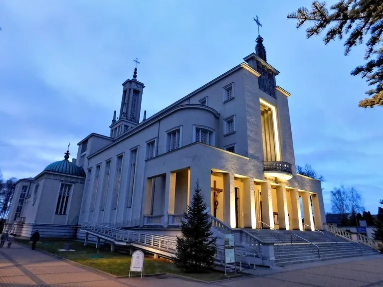 Bazylika w Niepokalanowie o zmierzchu, z oświetloną kolumnadą wejścia i wieżą zwieńczoną krzyżem