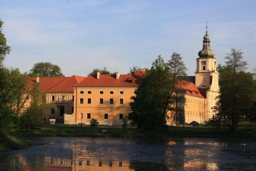 Barokowy zespół klasztorno-pałacowy w Rudach z cebulastą wieżą kościoła, odbijający się w stawie o zachodzie słońca