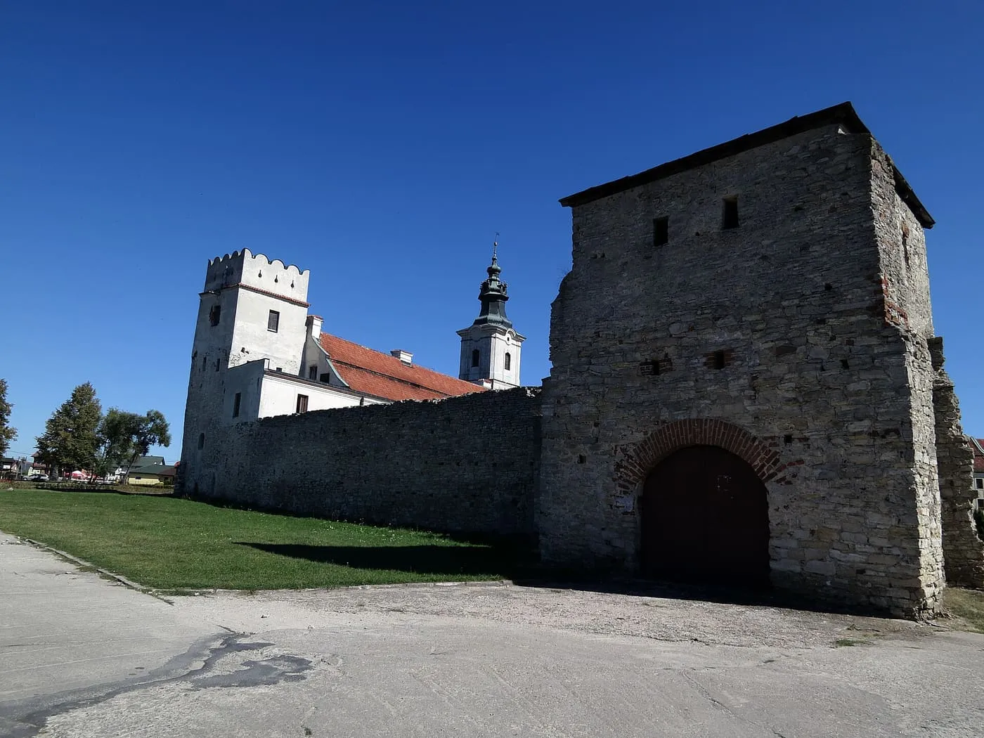 Warowne mury opactwa cystersów w Sulejowie z kamienną basztą bramną i wieżą kościoła w tle