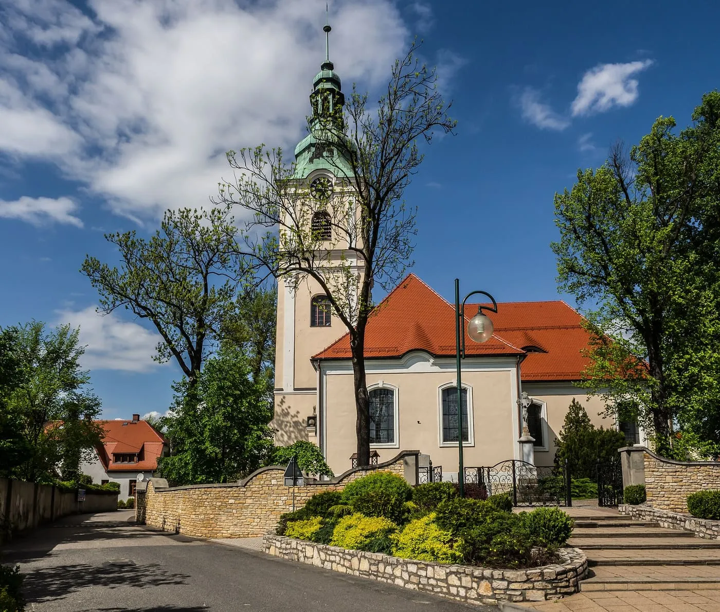 Neobarokowy kościół św. Jacka w Kamieniu Śląskim z wieżą zegarową zwieńczoną zielonym hełmem, za kamiennym murem