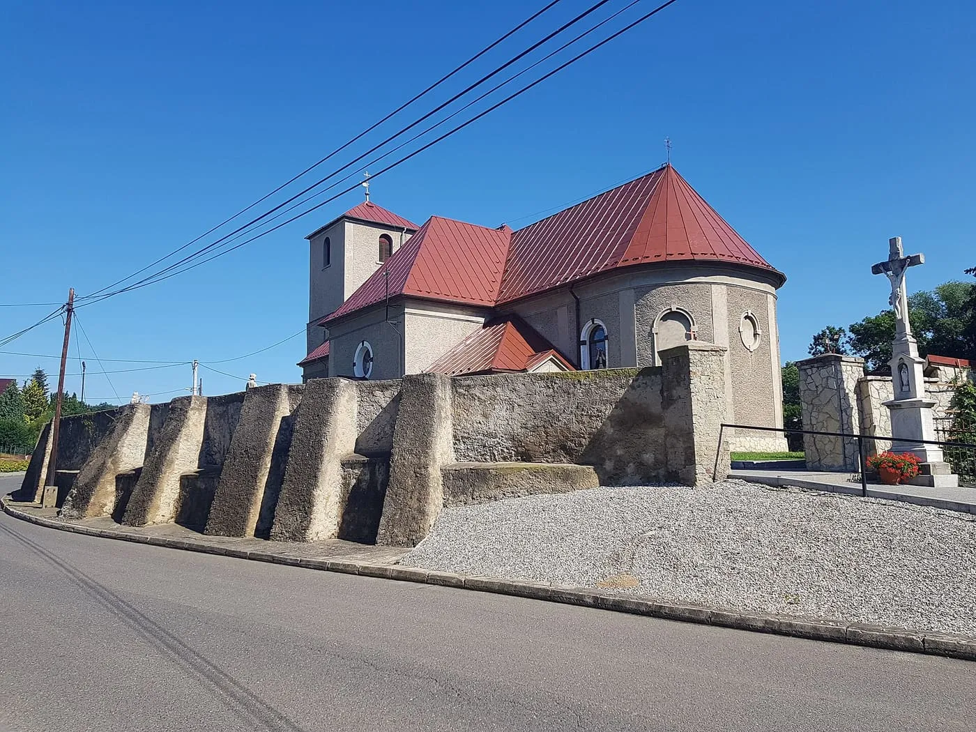 Kościół Trójcy Świętej we Włodzieninie z czerwonym dachem i przydrożnym krzyżem