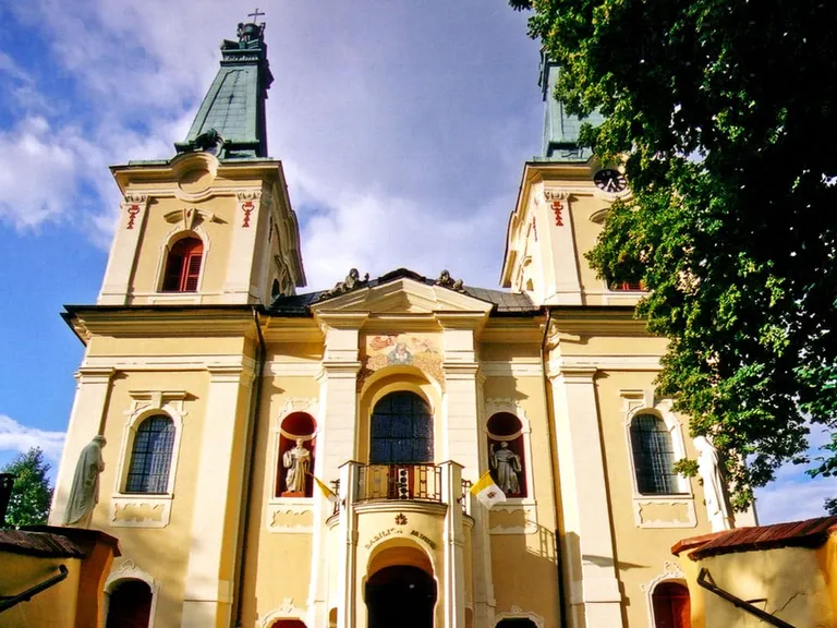 Żółto-biała barokowa fasada bazyliki w Rokitnie z dwiema wieżami zwieńczonymi zielonymi kopułami