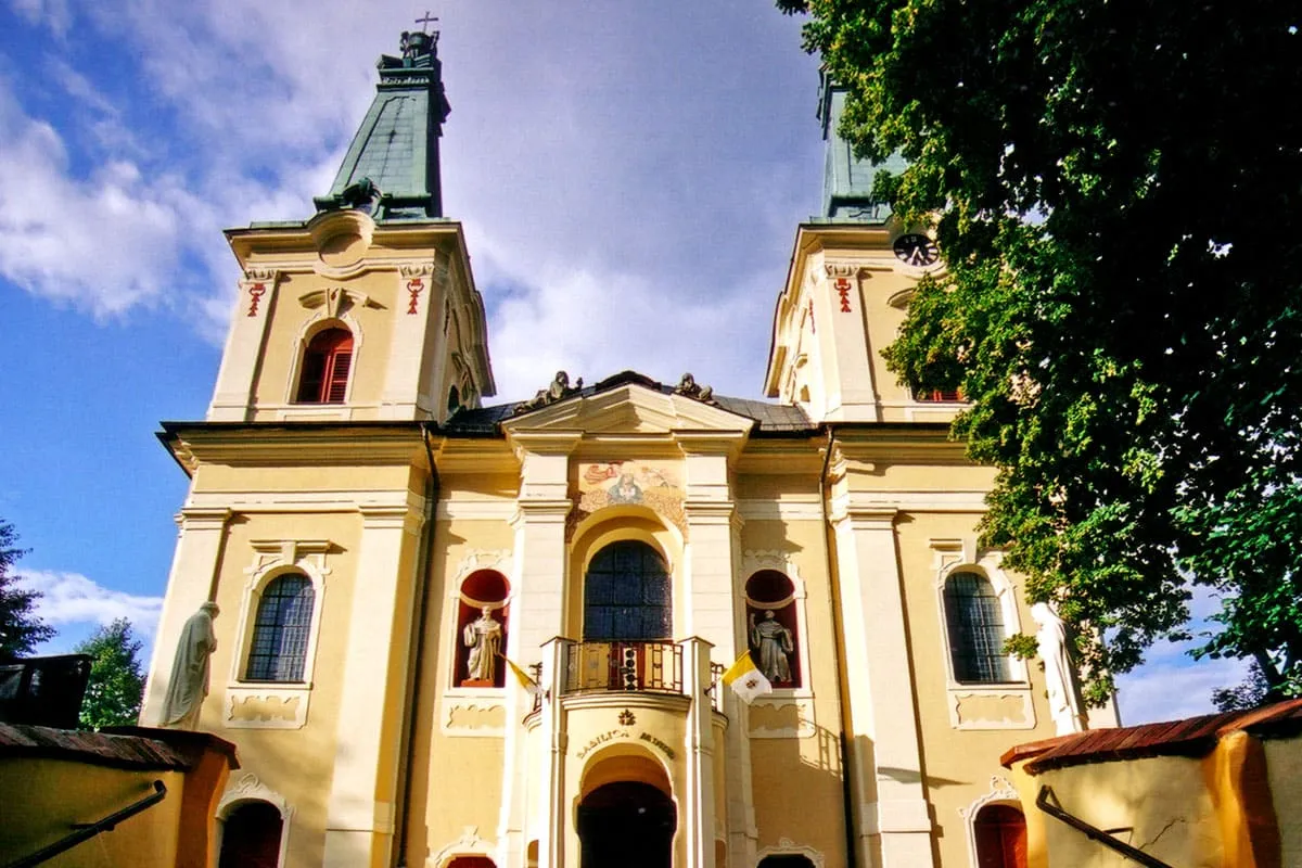 Żółto-biała barokowa fasada bazyliki w Rokitnie z dwiema wieżami zwieńczonymi zielonymi kopułami