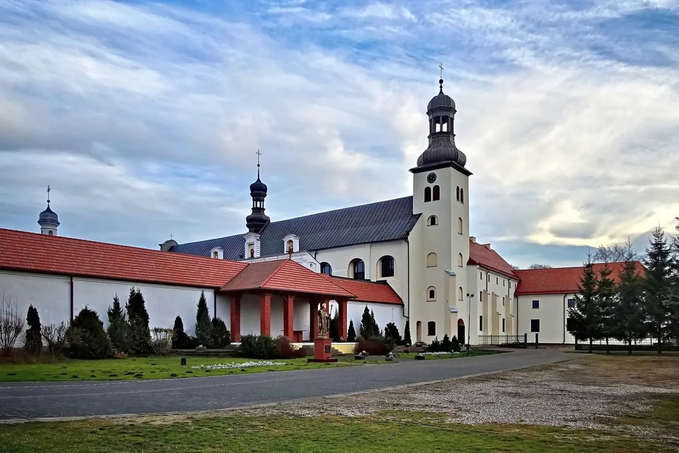 Biały klasztor bernardynów w Skępem z ciemnymi, cebulastymi wieżami i figurą świętego przed wejściem
