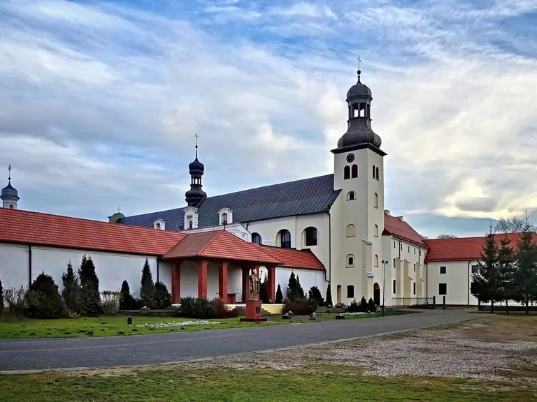 Biały klasztor bernardynów w Skępem z ciemnymi, cebulastymi wieżami i figurą świętego przed wejściem