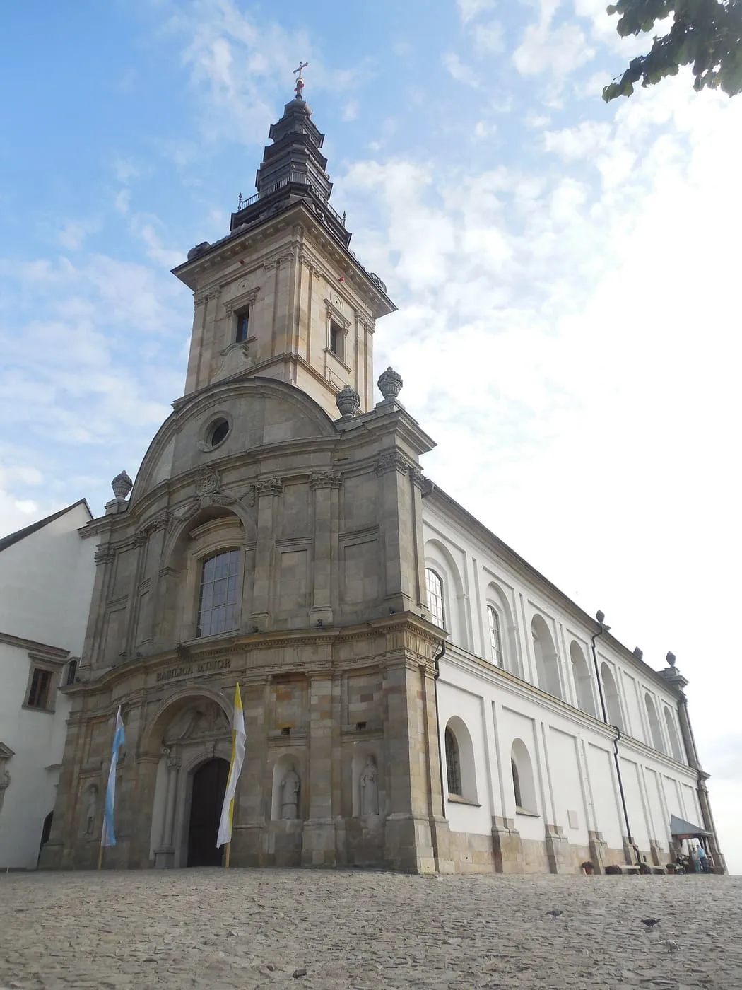 Barokowa fasada bazyliki na Świętym Krzyżu z wielopiętrową wieżą i napisem „Basilica Minor” nad wejściem