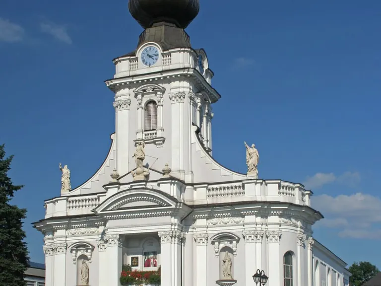 Biała, barokowa bazylika w Wadowicach z wieżą zwieńczoną czarną, cebulastą kopułą — kościół chrztu Jana Pawła II